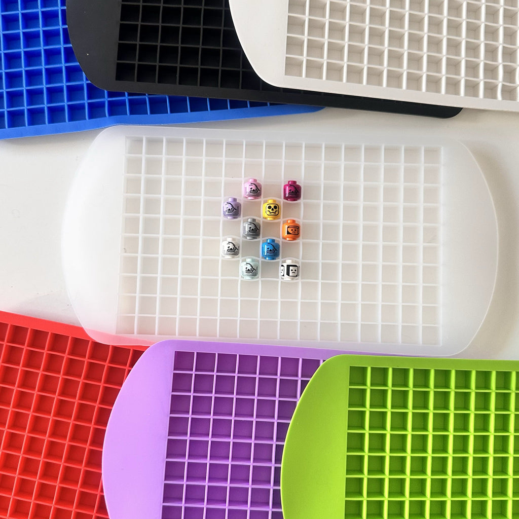 Silicone head holder trays in multiple colors with minifigure heads seated in the grid
